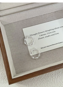 Detailed view of silver twisted hoop earrings on a beige fabric tray with decorative card