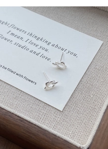 Macro shot of polished S925 sterling silver knot stud earrings on a minimalist card