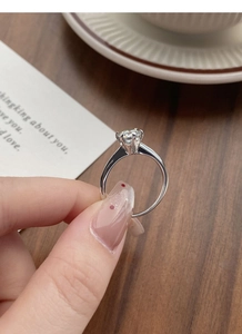 Classic six-prong round moissanite engagement ring held over a warm gift card