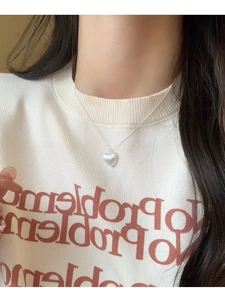 Dettaglio della collana con ciondolo a cuore perlato su un maglione bianco