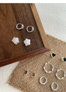 Detail of silver S925 earrings set with star, heart, and hoop designs on rustic wood