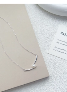 Macro shot of S925 silver necklace with white pearl on minimalist curved metal pendant