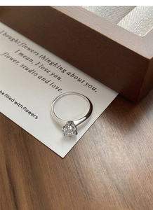 Close-up of a silver moissanite ring with six-prong setting on a rustic wooden box