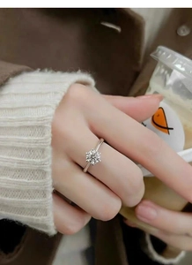 Detail of a one-carat moissanite ring with a six-prong setting on a hand holding a cup