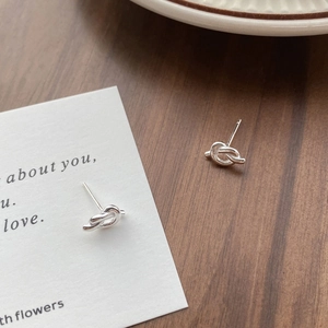 Minimalist S925 sterling silver knot stud earrings on a dark wood grain background