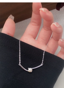 Detail of S925 silver cross necklace with freshwater pearl held against black fabric