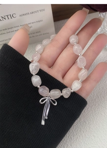 Detail eines rosa Kristall-Perlenarmbands mit silbernem Schleifenanhänger