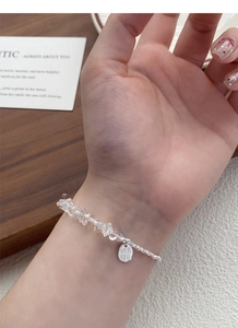 Detail of silver bracelet with clear crystals and Luck engraved tag on a woman's wrist