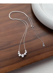 Detail of S925 sterling silver snake chain necklace with textured cat-eye beads on wood