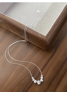 Detailed close-up of a silver snake chain necklace with bead charms on a wooden tray