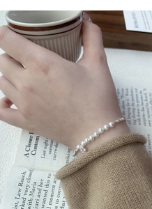 Detail of S925 sterling silver pearl bracelet with a sparkling diamond flower charm on wrist