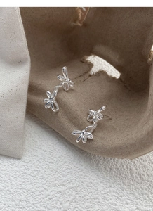 Detail of silver S925 double bow earrings on a minimalist textured neutral background
