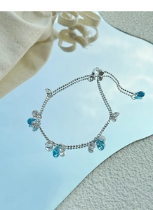 Adjustable silver bead bracelet with blue teardrop crystals over a sky mirror reflection
