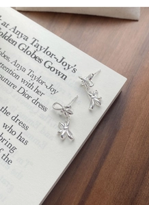 Macro shot of silver bow earrings on vintage magazine and dark wood surface