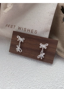 Detailed view of silver double bow dangle earrings on a natural wood and burlap background