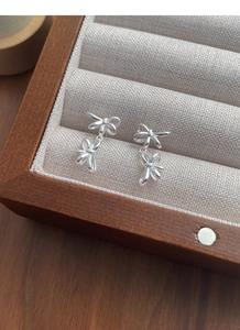Detailed view of elegant S925 sterling silver double bow earrings on rustic linen padding