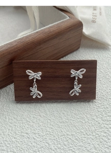Detail view of S925 sterling silver double bow dangle earrings on wooden display stand
