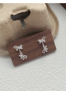 Detail of S925 sterling silver double bow drop earrings hanging on a wood base