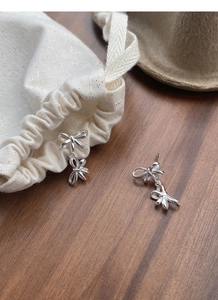 Close-up of double bow sterling silver earrings on dark wood surface with soft lighting