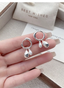 Detail view of 925 silver hoop earrings with waterdrop pearl and metal charms on gift bag