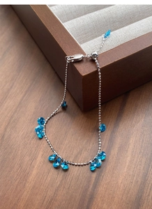 Macro detail of silver bead bracelet featuring blue teardrop crystal charms and slider clasp