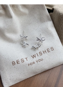 Detail of silver double bow stud earrings on a beige drawstring gift bag over wood
