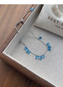 Detail of adjustable silver bracelet with light blue teardrop stones on a wooden tray