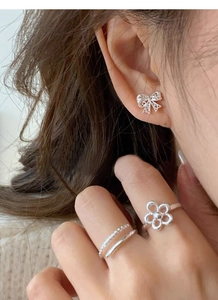 Dettaglio dell'orecchino a fiocco in argento S925 e anello floreale su modella in posa