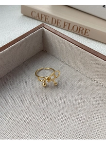 Detailed view of a gold bow ring with flowing lines and small gold beads on a tray