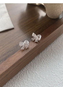 Dettaglio macro degli orecchini a fiocco in argento S925 su vassoio di legno