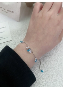 Detail of adjustable silver bracelet featuring blue teardrop zircon charms and fine bead chain