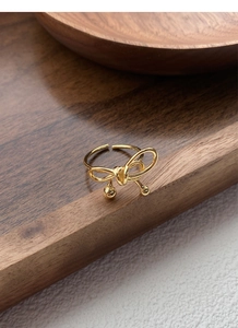 Detailed view of the gold woven bow ring featuring metallic bead accents on a wood surface