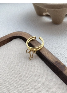 Macro shot of gold double-layer bow ring on linen tray showing fine polished metal texture