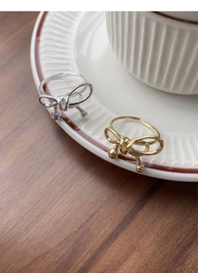 Close-up of silver and gold bow rings with dangling beads on white ceramic plate