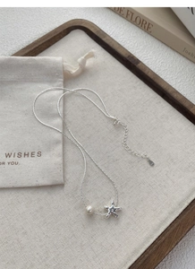 Détail du collier étoile de mer en argent S925 avec perle sur plateau en lin et sac