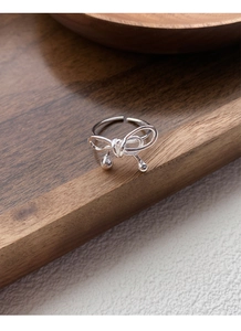 Macro detail of S925 silver bow ring with hanging beads on a rustic wooden stand
