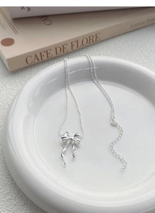 Gros plan du pendentif nœud en argent avec chaîne à billes sur plat en céramique