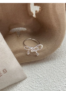Macro shot of silver bow ring with woven lines and dangling beads on natural fabric
