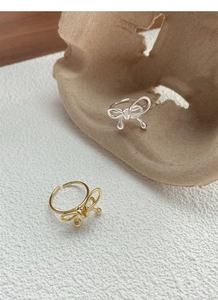 Detail of silver and gold bow rings with small bead accents on a textured background