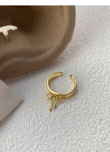 Detailed shot of an adjustable gold bow ring on a white textured minimalist surface