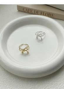 Detailed view of woven bow rings in gold and silver finish on a ceramic tray