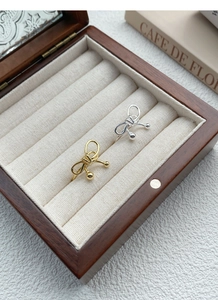 Detail of silver and gold woven bow rings with bead accents inside a premium wooden jewelry box