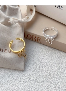Detail of elegant S925 silver bow rings in gold and silver finish on a soft fabric