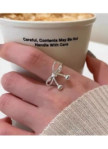Detailed close-up of a silver bow ring with round beads on a model hand with a coffee cup