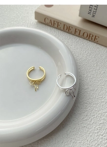 Detail of gold and silver bow-knot rings on white ceramic plate with a minimalist background