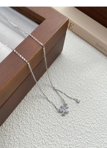 Detailed close-up of a silver flower pendant necklace with zircons on a wooden jewelry box