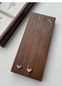 Detail view of heart-shaped S925 sterling silver necklaces on a dark wood display stand