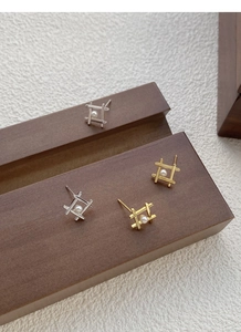 Macro shot of gold and silver S925 geometric pearl stud earrings on a wooden box
