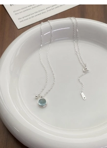 Detail of S925 sterling silver chain with round light blue gemstone pendant in ceramic dish