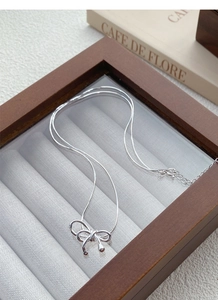Détail du collier pendentif nœud en argent avec chaîne serpent dans un écrin en bois